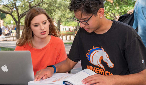 Two students look at a laptop computer.