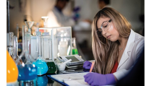 Student doing research, wearing goggles, holding vial.