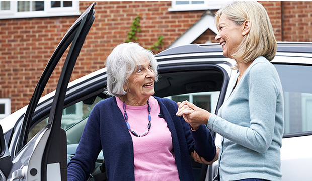 Older woman being helped out of car by middle-aged woman