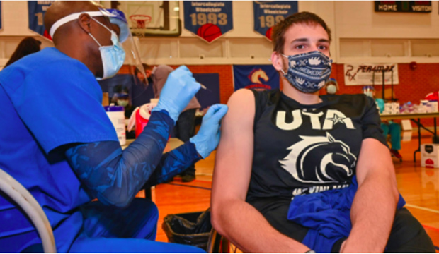 Male student receiving COVID-19 vaccine at UTA's Physical Education building.