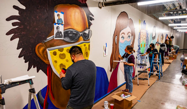 Artists painting mural of people wearing face masks.