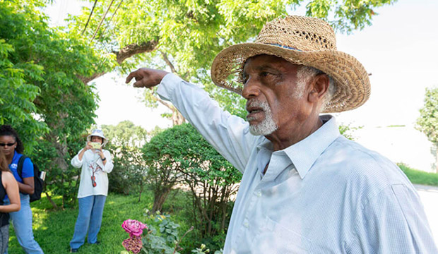 Older Black man wearing a straw hat pointing at something.