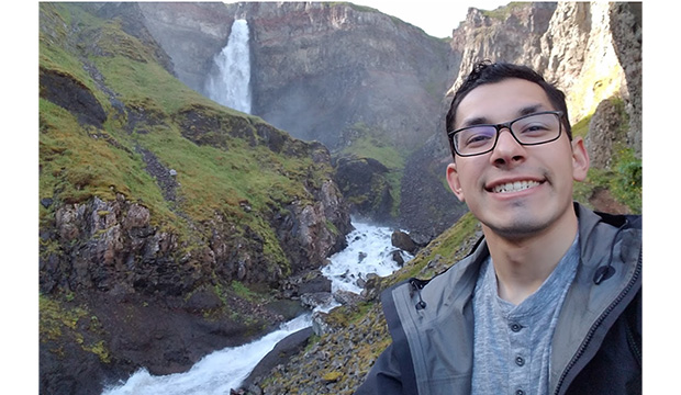 Study Abroad student with mountainous scene with waterfall in background.
