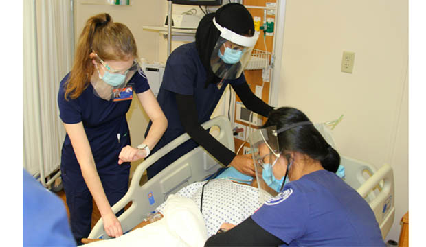 Masked nursing students working on a manikin.