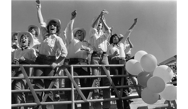Students in western attire and cowboy hats cheering at Homecoming 1985.