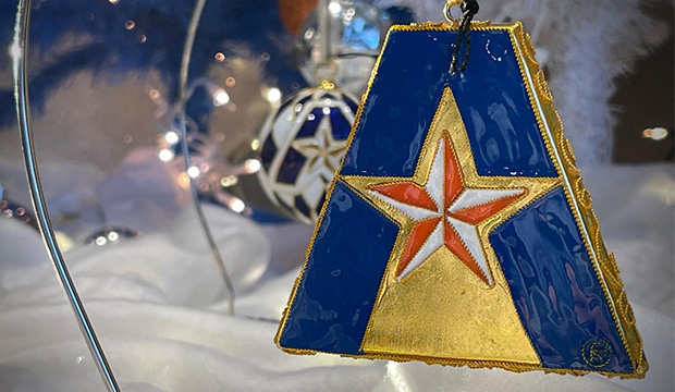 Christmas ornament in shape of UTA "A" logo with blue A and orange and white star in middle, all with a gold background.