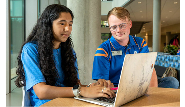 A female student works on a laptop computer white a male student looks at the screen.