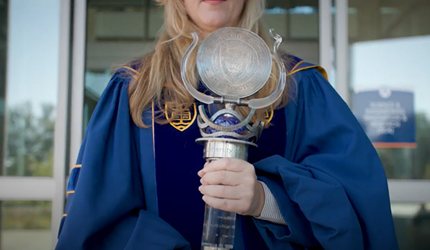 Woman in commencement regalia holds the UTA mace.