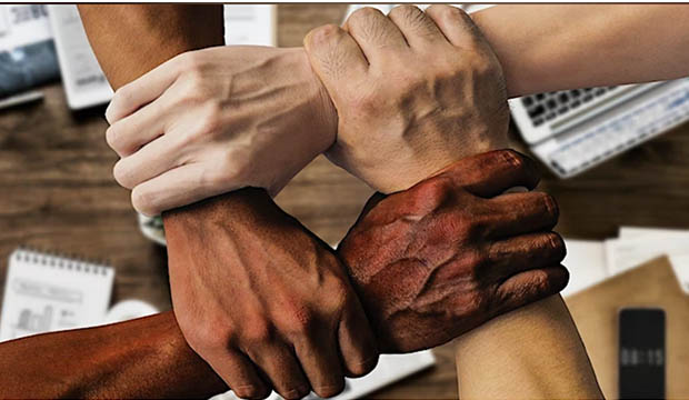 Four male hands, each of difference color/race, interlocked with one another.