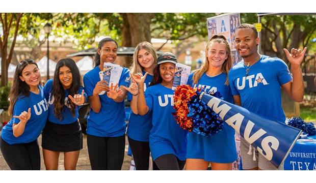 Seven students wearing blue UTA shirts give the Maverick hand sign.