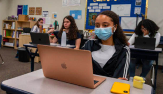 Students in classroom, some masked and some not masked.