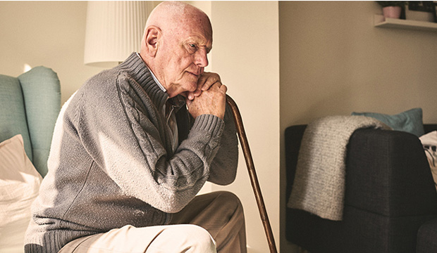 Elderly man sitting and leaning on cane.