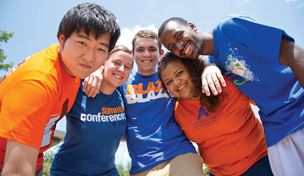 Five students in UTA blue and orange shirts huddle together.