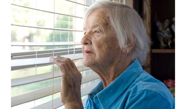 Elderly woman looking through window blinds.