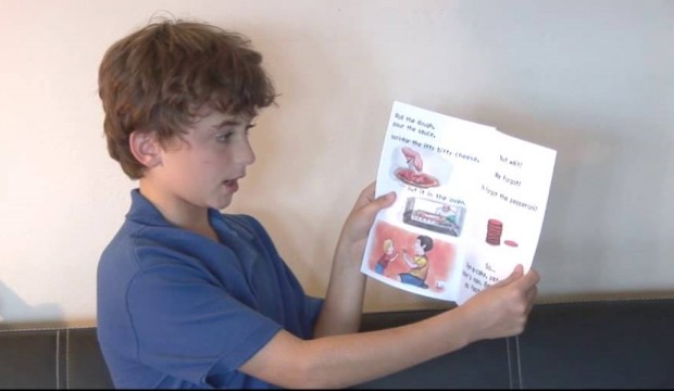 Boy showing reading book to computer screen