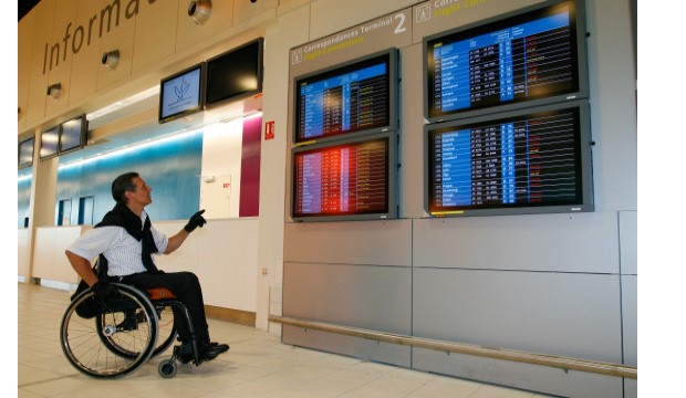 Man in wheelchair at airport terminal looking at flight arrival board