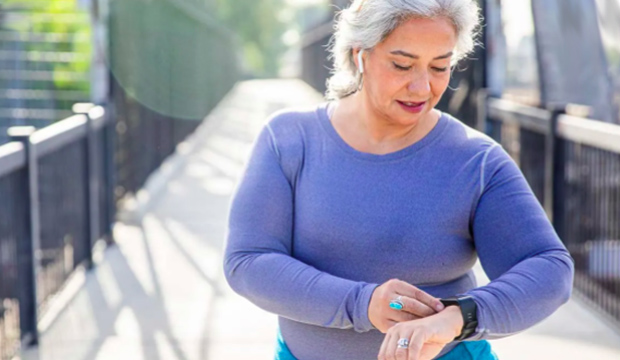 Woman with gray hair wearing exercise clothing looks at her FitBit.