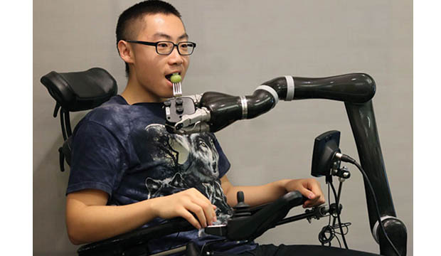 Man with in wheelchair with robotic are feeding him.