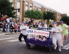 Students pushing a wheeled bed down Pecan street.
