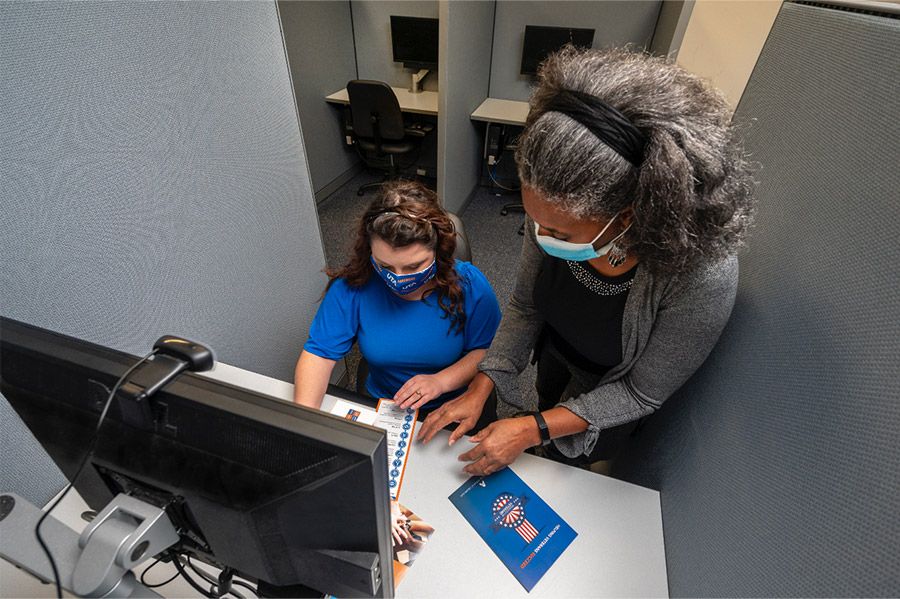 Elvira Smith assists Faith Magness (seated).